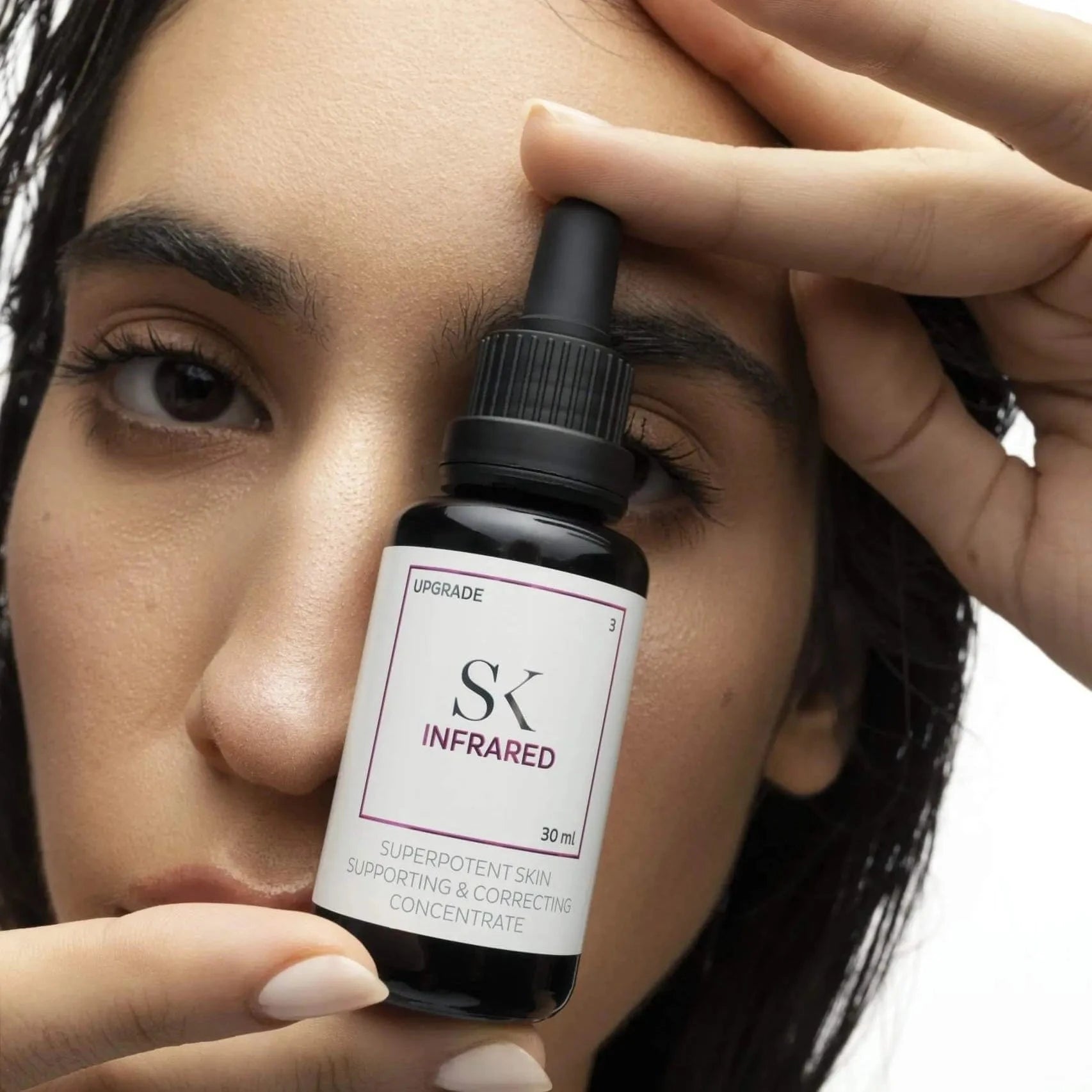 Person holding a bottle of SK Infrared skincare concentrate near their face.