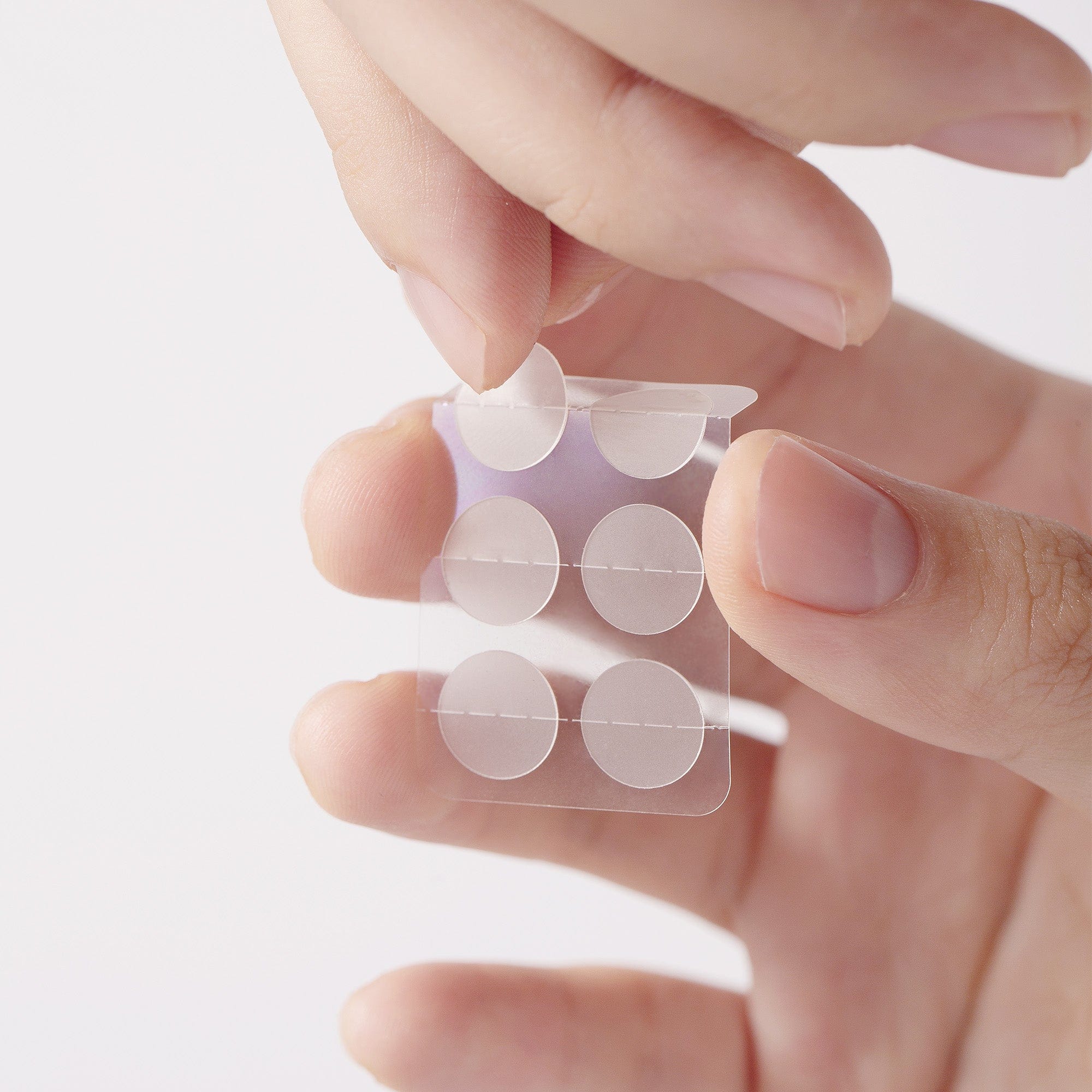 Hand holding a small transparent packaging with circular items against a light background